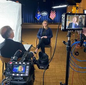 Marleigh Young sitting opposite a Justice Department employee surrounded by lights, cameras and microphones.